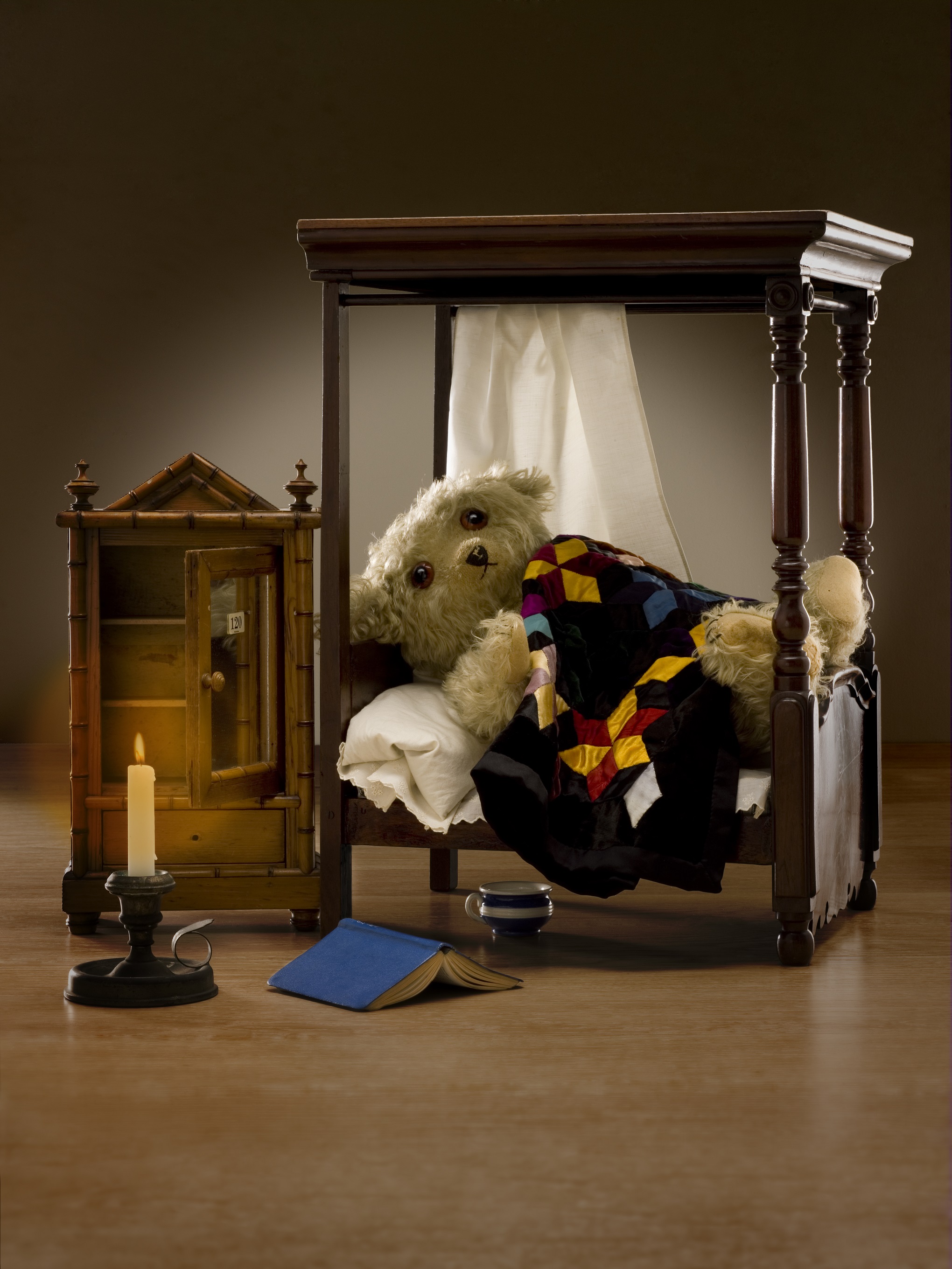 A bedroom scene with a doll's four-poster bed with a teddy bear